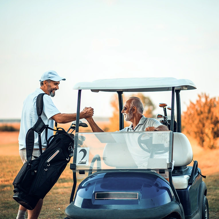 Two men shaking hands in a golf cart on a golf course.